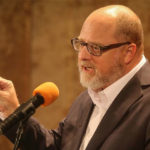 Adam Kahane speaks at a microphone. 